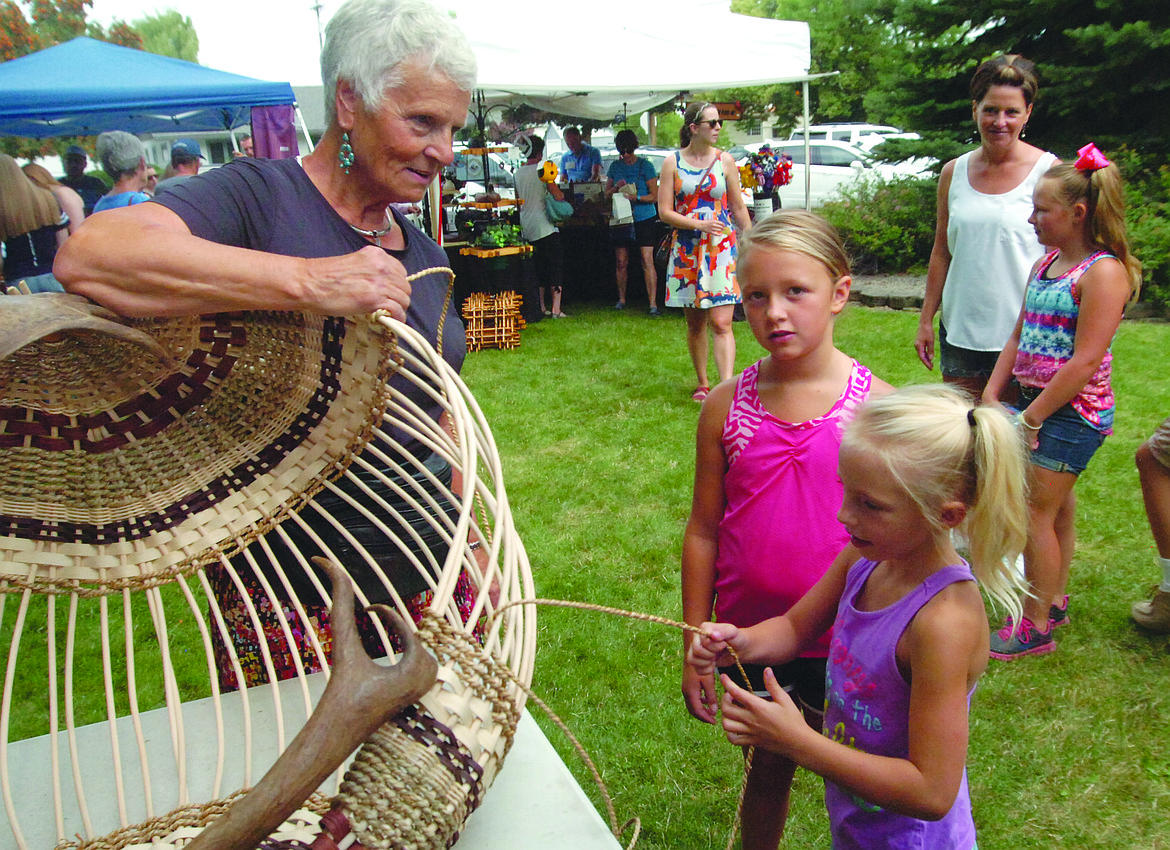 GITTI MILLER watches as Brinlee Reum weave a caribou basket at Miller&#146;s booth during the Sandpiper Art Festival on the Lake County Courthouse lawn last Saturday. Brinlee&#146;s sister Anna is next to do some weaving. (Joe Sova photos/Lake County Leader)