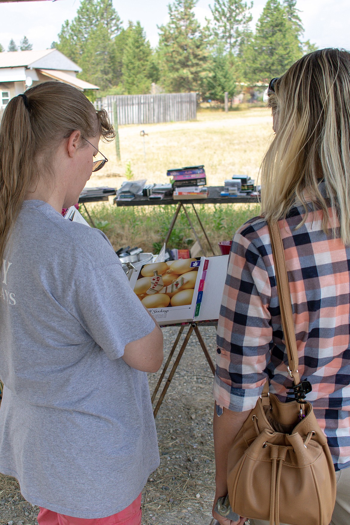 Katy Cockerham and Tammy Wallace look through a book of Christmas cross stitching Saturday at the yard sale to benefit the Lincoln County Student Stand Down that will take place Monday, August 20 at 4 p.m. (Ben Kibbey/The Western News)