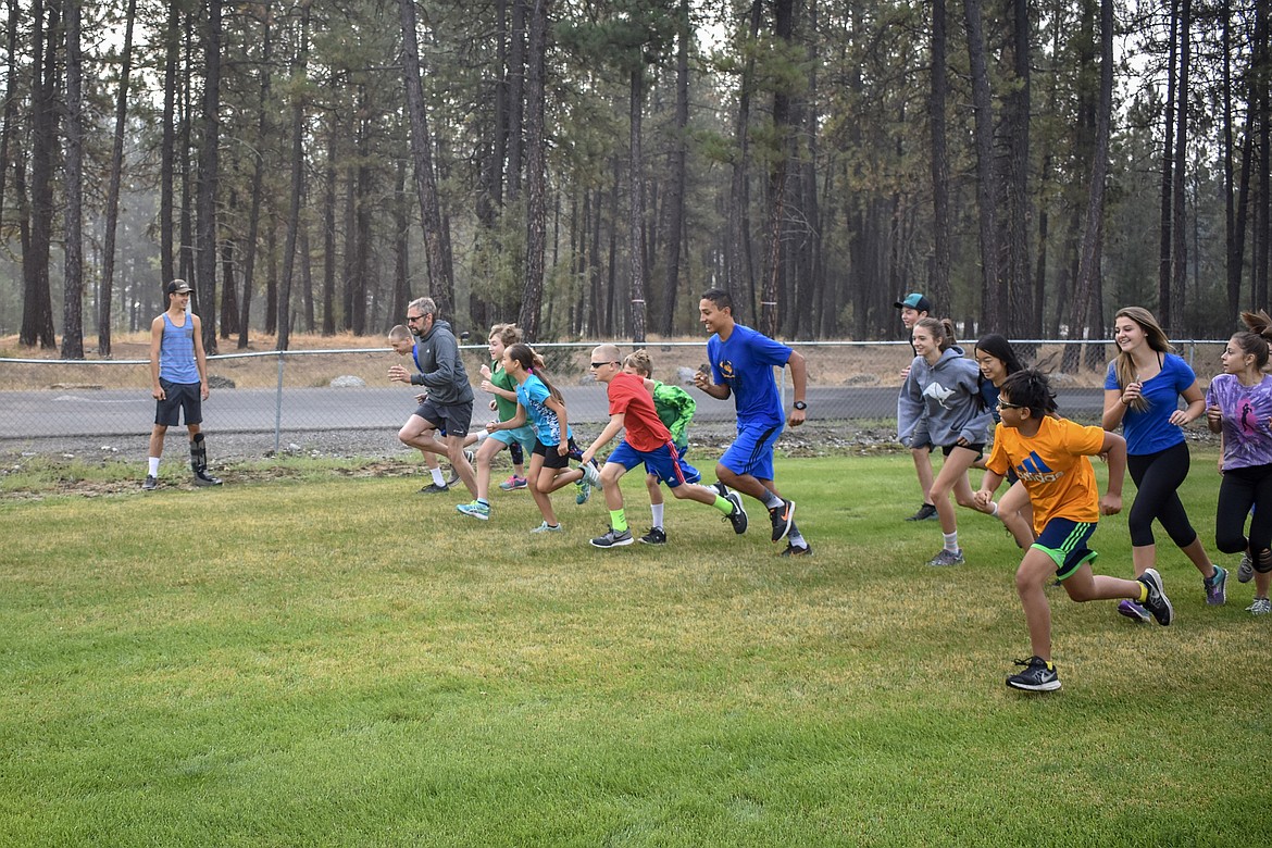 Coach Rodd Zeiler leads the Logger high school and middle school cross country teams in a motivational crossing of the finish line during practice on Aug. 17. (Ben Kibbey/The Western News)