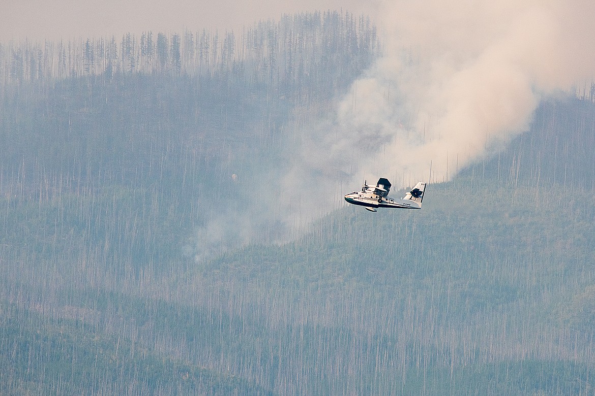 A super scooper plane flies past a plume on the Howe Ridge Fire en route to an area near the Inside North Fork Road where firefighters are looking to hold the line.