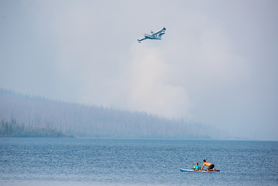 A man and child watch the super scooper planes from a paddle board on Lake McDonald Wednesday.