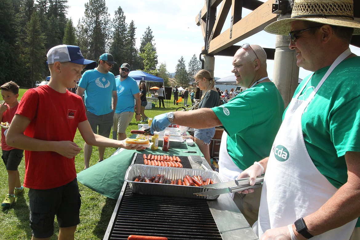 Wes Veach of bankcda serves a complimentary hot dog to Jackson Frickle, 12, of Post Falls, during the inaugural COEURfest in McEuen Park on Saturday. Veach and Mark Beardsley, right, reported that more than 700 free hot dogs were served to community members during the event.