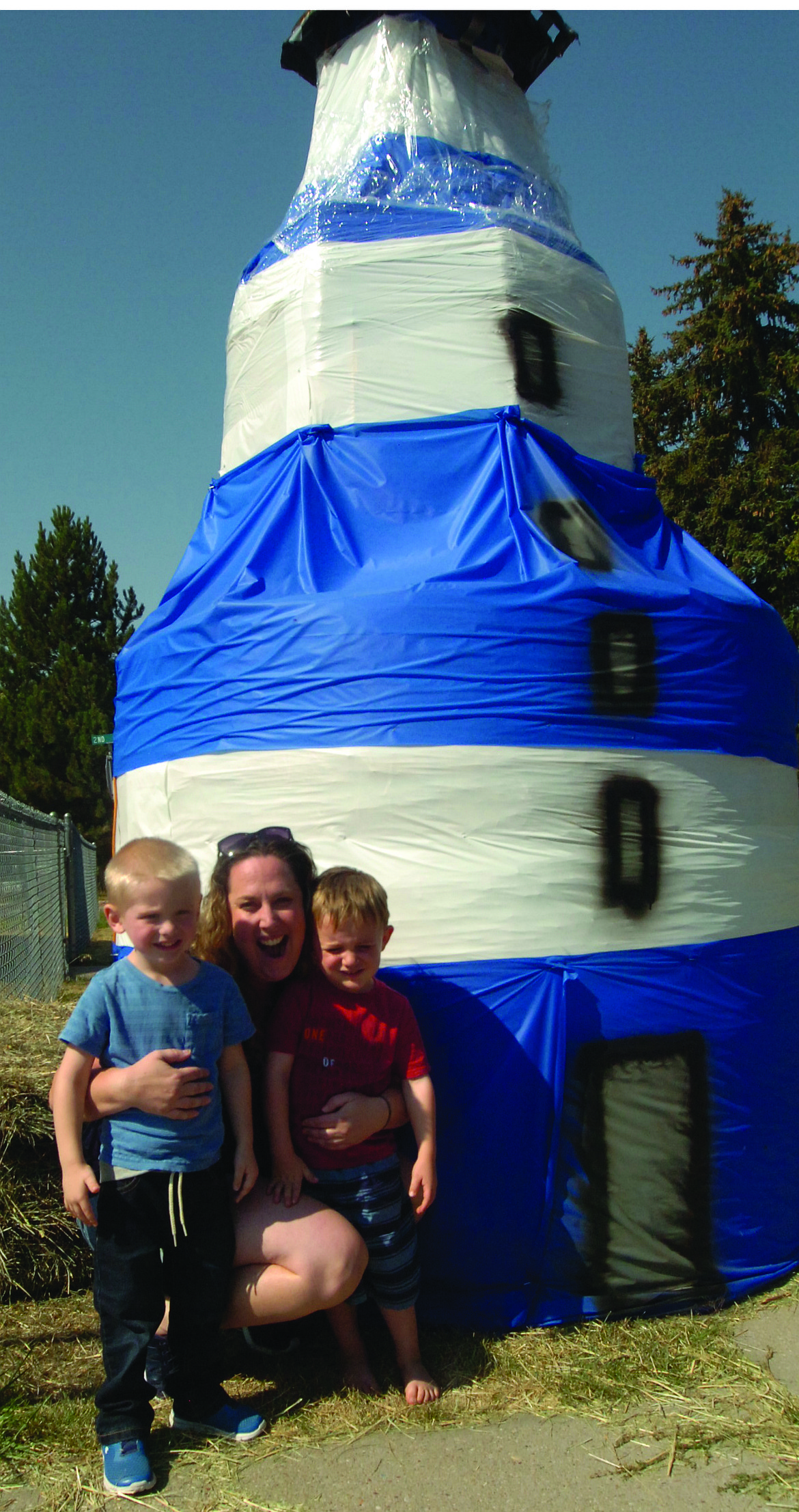 Angela Nicholas are pictured with Dex, left, and Sam in front of the Lighthouse Christian Fellowship Church Trail of Bales exhibit in Ronan.