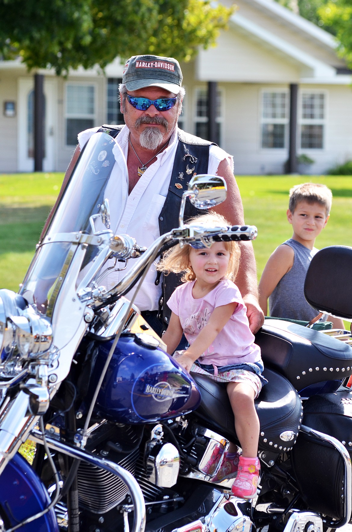Plains local Buck Larson helped young Cadence Hedahl onto his Harley so she could get a photo on her favorite bike at the show. (Erin Jusseaume/Clark Fork Valley Press)