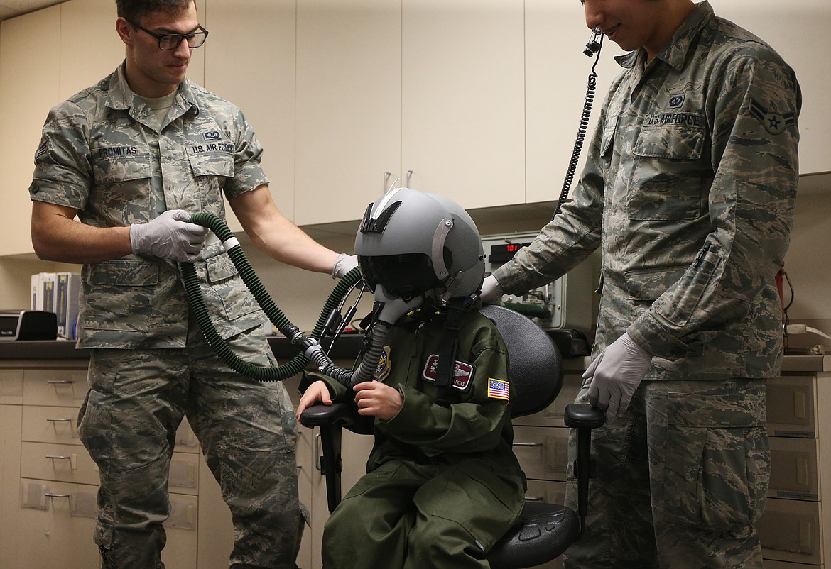 Zach Promitas, left, Sr. Airman, and Salvador Solis, Airman First Class, help 7-year-old Isaiah Watkins try on a fighter pilot helmet during Isaiah&#146;s Pilot for a Day visit to Fairchild Air Force Base outside Spokane on Friday. (LOREN BENOIT/Press)