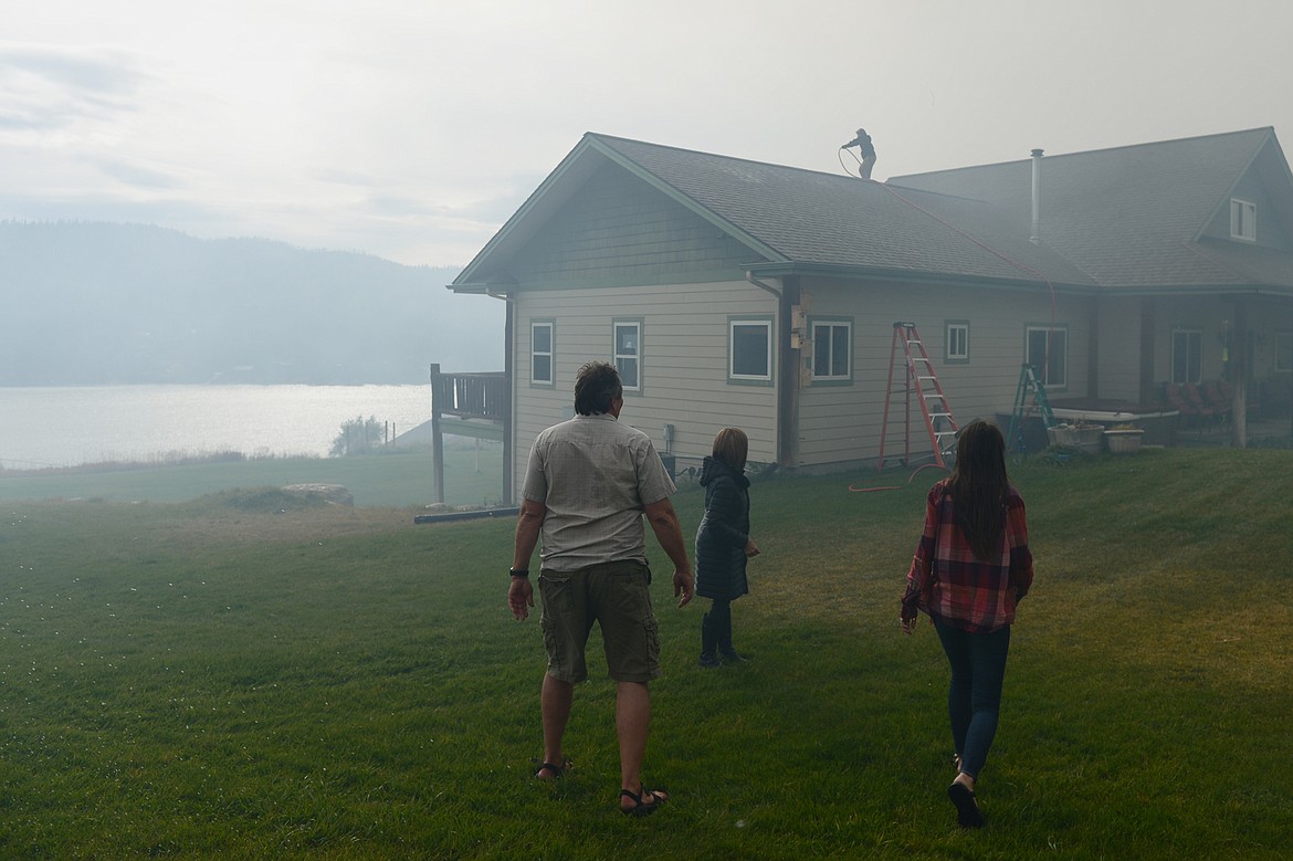 Residents along Roybals Way near Foys Lake spray their house and roof with water after a fire started in an adjoining field on Tuesday. (Casey Kreider/Daily Inter Lake)