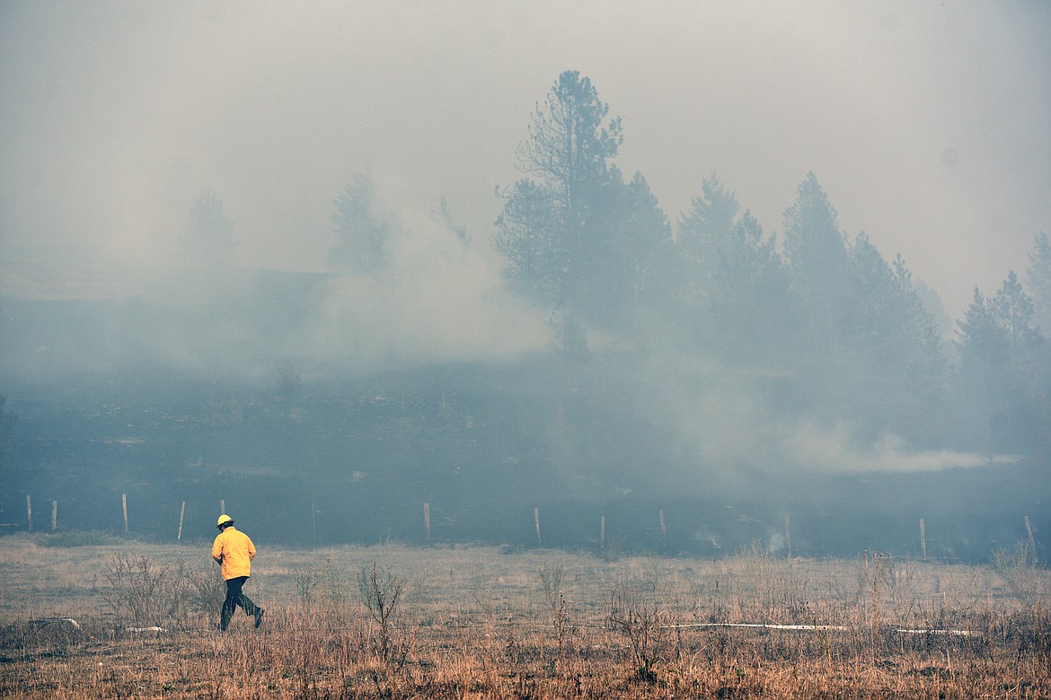 A firefighter walks through an unburned portion of a field that caught fire off Foys Lake Road in Kalispell on Tuesday. (Casey Kreider/Daily Inter Lake)