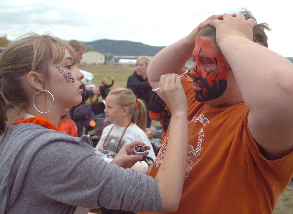 Plains High School sophomore Justine Martin paints the face of eighth grader Ryan Collette in orange and black school colors at the football field before the Horsemen Homecoming game. (Joe Sova/Clark Fork Valley Press)