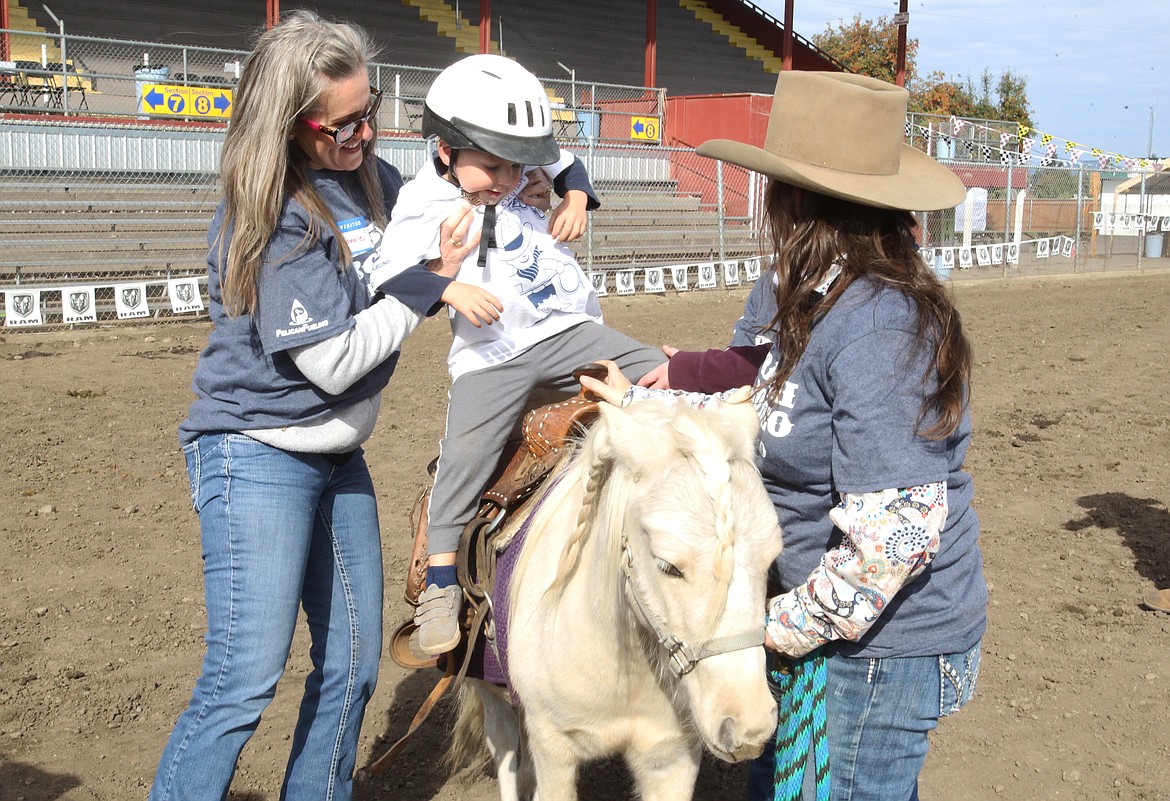 Rascal Rodeo volunteer Bonnie Martinelli helps 4-year-old Skylan Burns get saddled up with assistance from volunteers Cinniman Thomas, right, and Melanie Rabelle, 11 (behind Thomas). The fifth annual Coeur d'Alene Rascal Rodeo welcomed about 50 special needs participants to the arena at the Kootenai County Fairgrounds, where they rode horses, lassoed small model bulls and engaged in other Western-themed activities. (DEVIN WEEKS/Press)