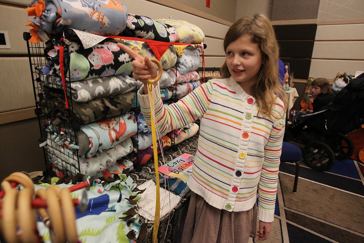 Aderyn Marker, 11, of Coeur d&#146;Alene, points to an image of kids using hand kites, like the one she&#146;s holding, on Sunday during the Coeur d&#146;Alene Makers Market in The Coeur d&#146;Alene Resort. Hand kites are a simple toy of wooden rings and ribbon. Aderyn sells them and cozy tied blankets through Aderyn&#146;s Rainbow Creations. (DEVIN WEEKS/Press)