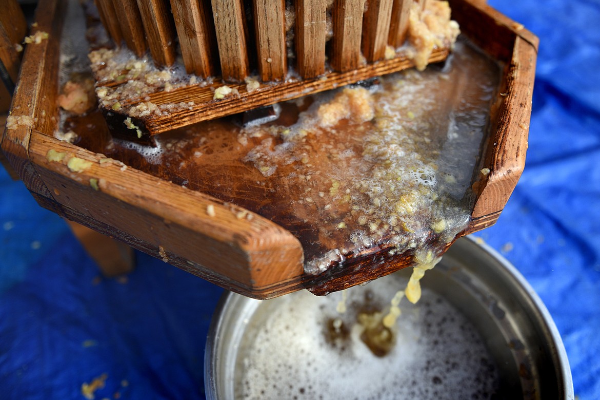 Unpasteurized cider and bits of apple are collected from a press.