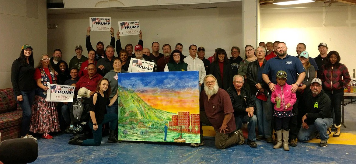 Dave Williams, with assistance from Plains High School freshman Haylee Steinebach, painted this depiction of President Donald Trump saluting the Afghanistan and Iraqi War Memorial in Missoula. In the photo, Williams with a beard and Steinebach are kneeling on either side of the painting. (Photos courtesy of Dave Williams)