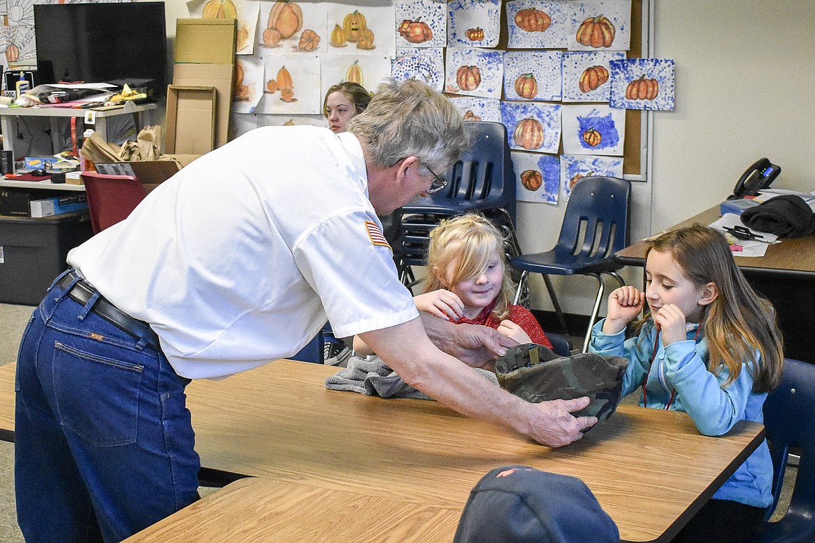 VFW John E. Freeman Post 5514 quartermaster Jerry Erickson shows a U.S. Army kevlar helmet to W.F. Morrison Elementary students Grace Steiger and Aisha Leighty during a visit local veterans made to the school Thursday. (Ben Kibbey/The Western News)