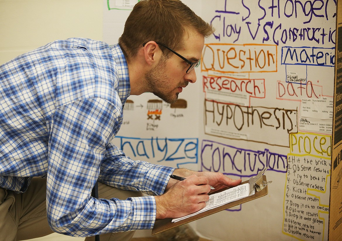 Thomas Staples, an assistant principal at Canfield Middle School, writes notes on a sheet of paper as he judges the sixth-grade science projects on Wednesday afternoon. (LOREN BENOIT/Press)