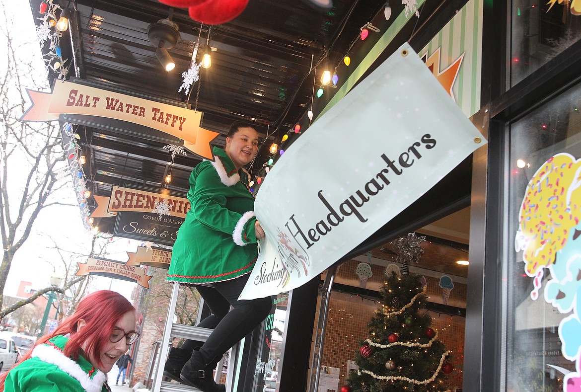 Shenanigans Sweets and Treats assistant manager Alexis Nelson, left, helps store manager Mallary Juarez hang a sign on the front of the downtown Coeur d'Alene store during Small Business Saturday to let shoppers know Shenanigans is the &quot;Stocking Stuffer Headquarters.&quot; Many shops downtown put out special signs and balloons to bring in customers to support local businesses during this busy shopping weekend. (DEVIN WEEKS/Press)