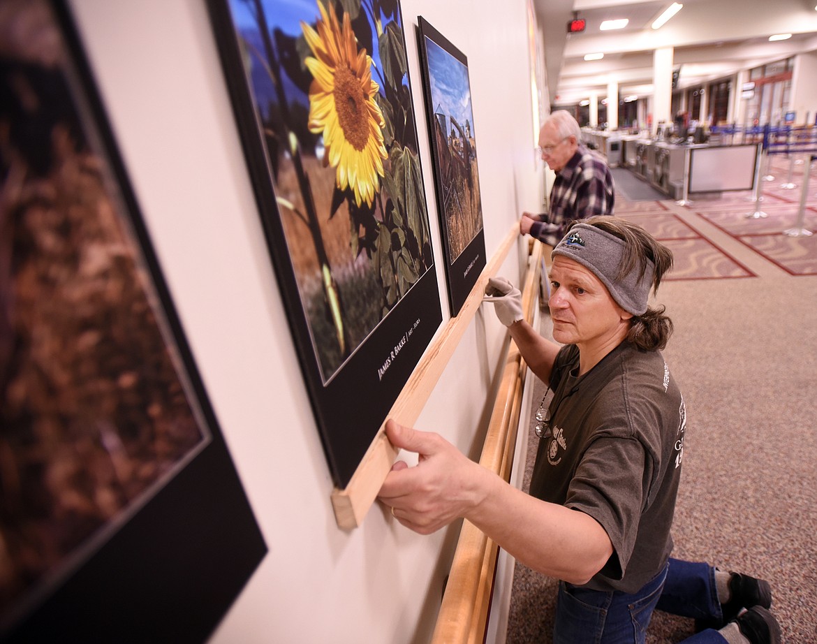 Bret Bouda and Terry Abell hangs work by James R. Bakke at the Glacier Park International Airport on Nov. 19. (Brenda Ahearn/Daily Inter Lake)