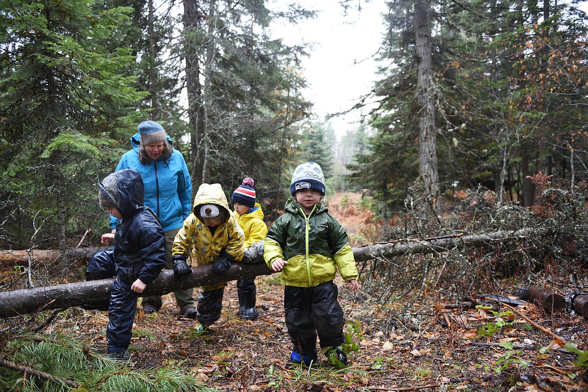 Students climb over a fallen tree with teacher-assistant Jean Kramer during a hike at Foxtail Forskola.