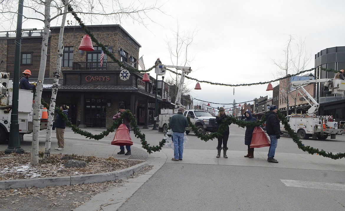 Volunteers hold a section of garland Sunday morning on Central Avenue. (Heidi Desch/Whitefish Pilot)