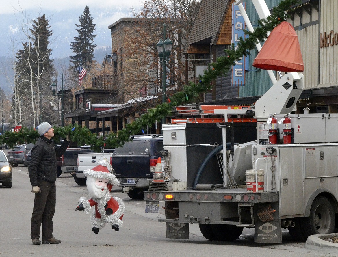 Chris Schustrom holds up Santa as the garland is lifted into the air on Central Avenue Sunday morning. (Heidi Desch/Whitefish Pilot)