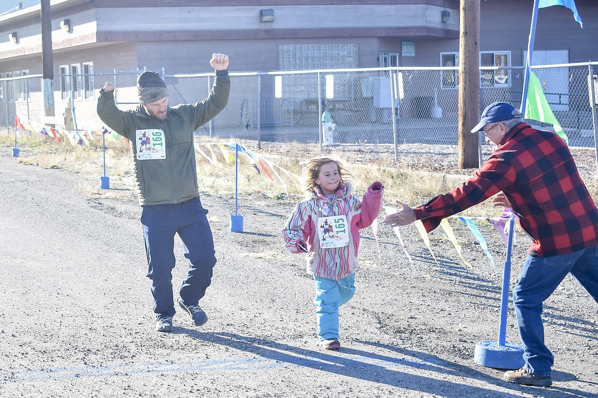 Mya Sloan goes for a high-five as she and Adam Sloan cross the finish line during the Turkey Dash 5k fun run. (Ben Kibbey/The Western News)