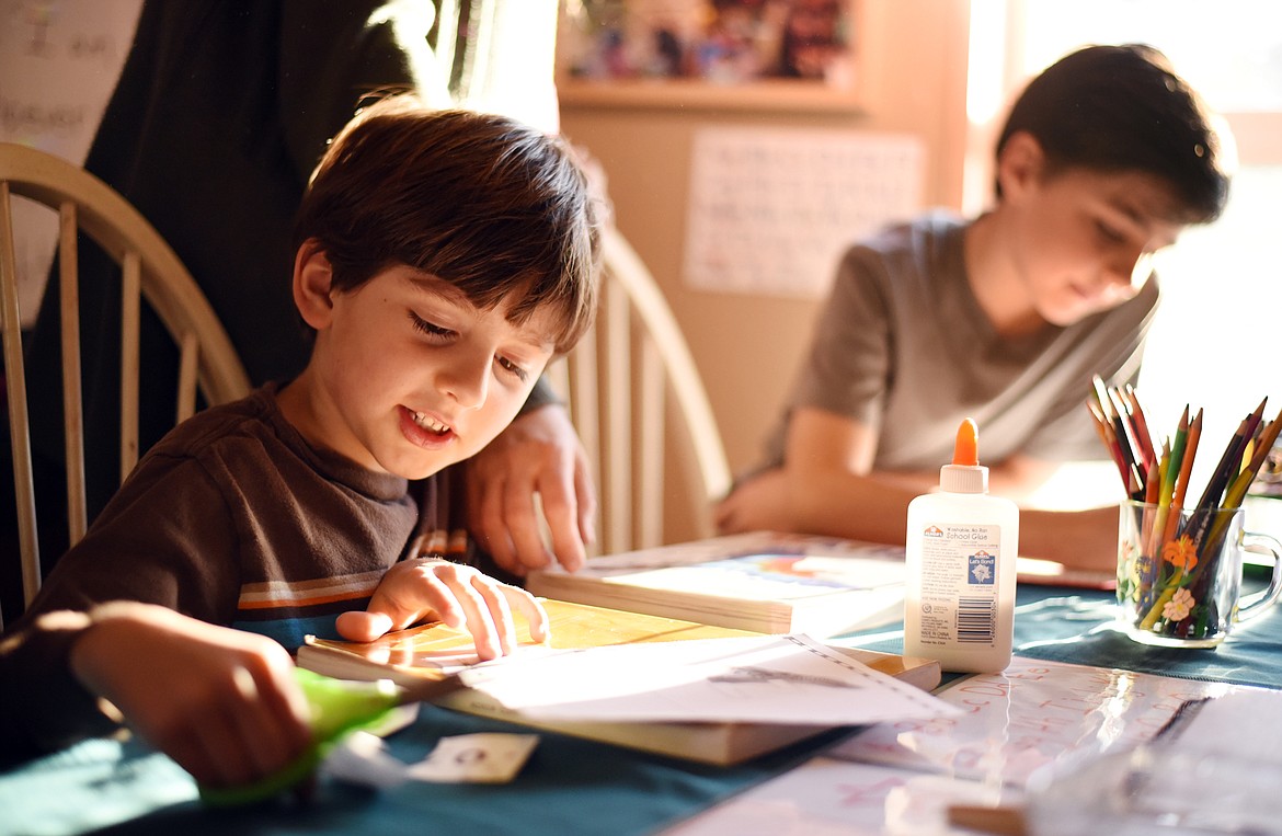 Gideon Clark, 5, works on a home-school project that combines letters and art as he and his brothers study together. In the background his brother Jubal works on a math assignment. (Brenda Ahearn/Daily Inter Lake)