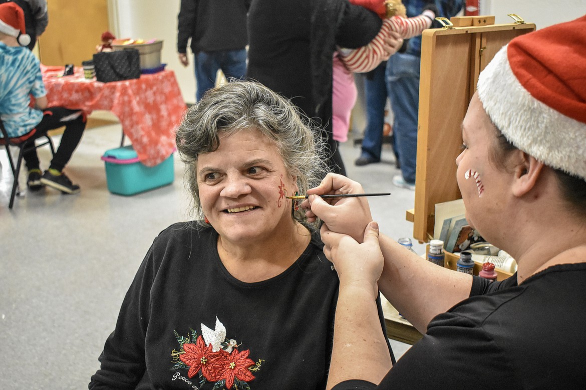 Tabitha Viergutz paints Judy Hutchison at Libby VFW Post 1548 Sunday during the Lincoln County Christmas Annual Toy Giveaway. Hutchison was trying to encourage her granddaughter Crystalina Noble to get her face painted. (Ben Kibbey/The Western News)