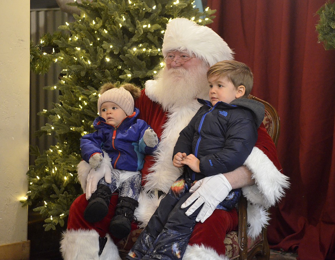 Stella Alcott, 10 months old, and Micah Alcott, 3, sit on Santa&#146;s lap Friday evening at Stumptown Marketplace during the annual Whitefish Christmas Stroll. (Heidi Desch/Whitefish Pilot)