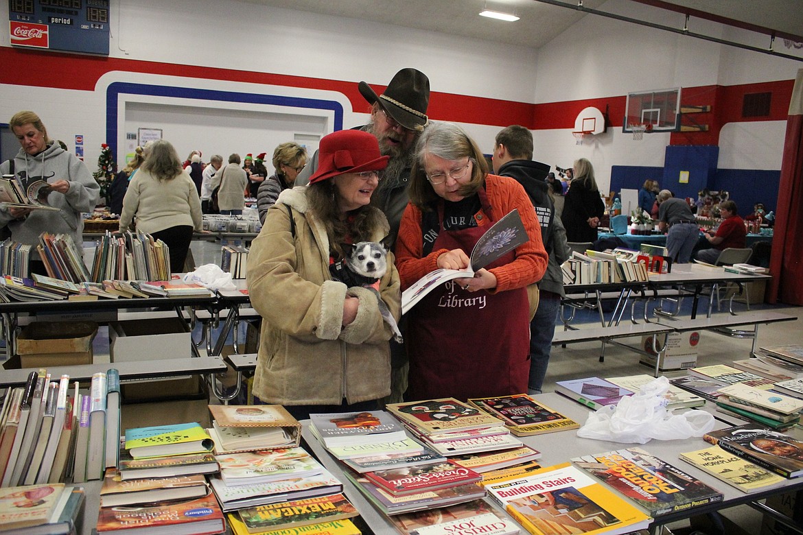 Mineral County Library Director Guna Chaberek shares a book with Griz and Pauley Wilson along with their service dog, Chrissy, at the library&#146;s annual holiday fundraiser on Dec. 8.