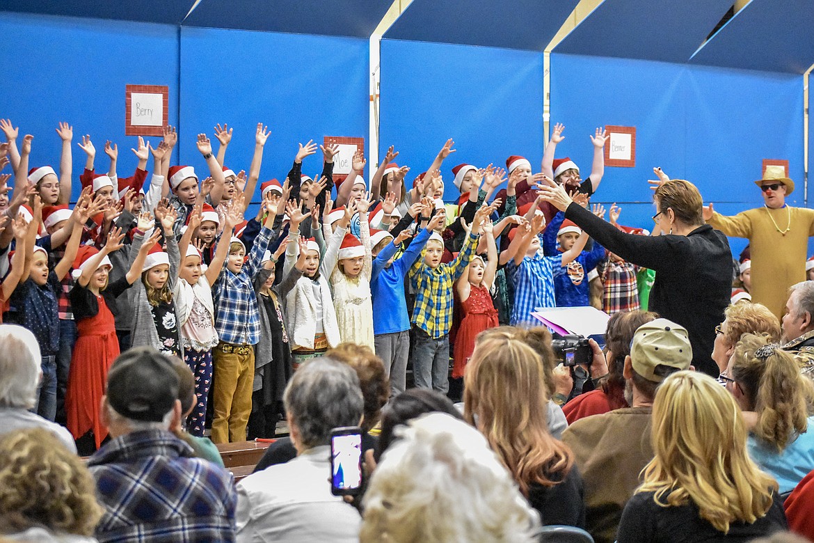With a little help from reindeer and art teacher Kyle Hannah, Libby Public Schools music teacher Lorraine Braun leads 4th and 5th grade students in song during their Christmas concert at the Libby Elementary School gym Thursday. (Ben Kibbey/The Western News)