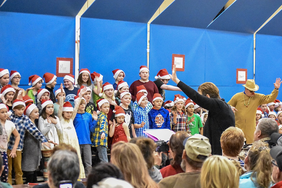 With a little help from reindeer and art teacher Kyle Hannah, Libby Public School music teacher Lorraine Braun leads 4th and 5th grade students in song during their Christmas concert at the Libby Elementary School Gym Thursday. (Ben Kibbey/The Western News)