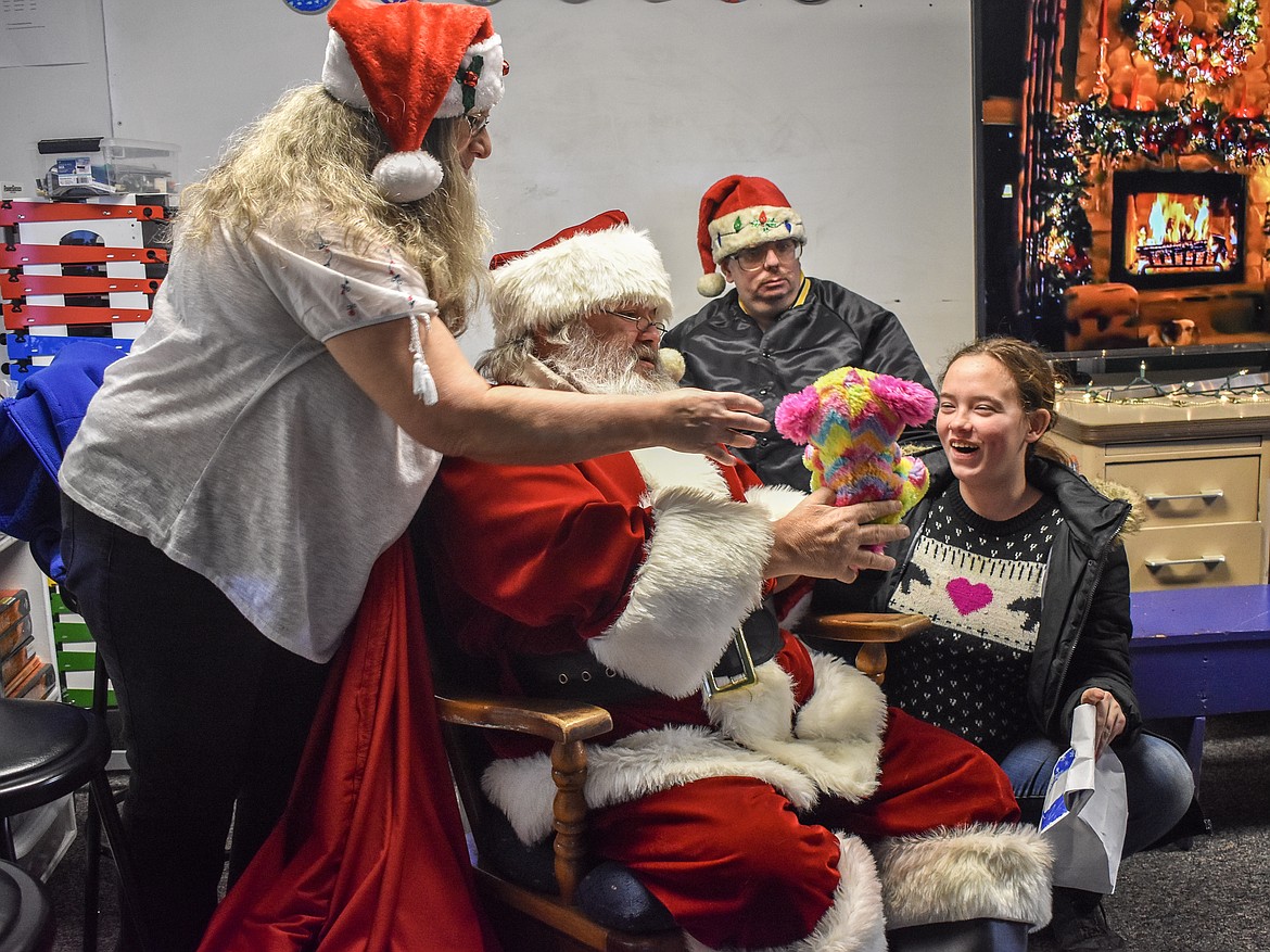 Assisted by Troy VFW Post 5514 Auxiliary President Francine Ninneman, Santa gives 8th grader EmmaLea White-Carlson a rainbow-colored stuffed animal for Christmas at the McCormick Elementary School on Friday. (Ben Kibbey/The Western News)