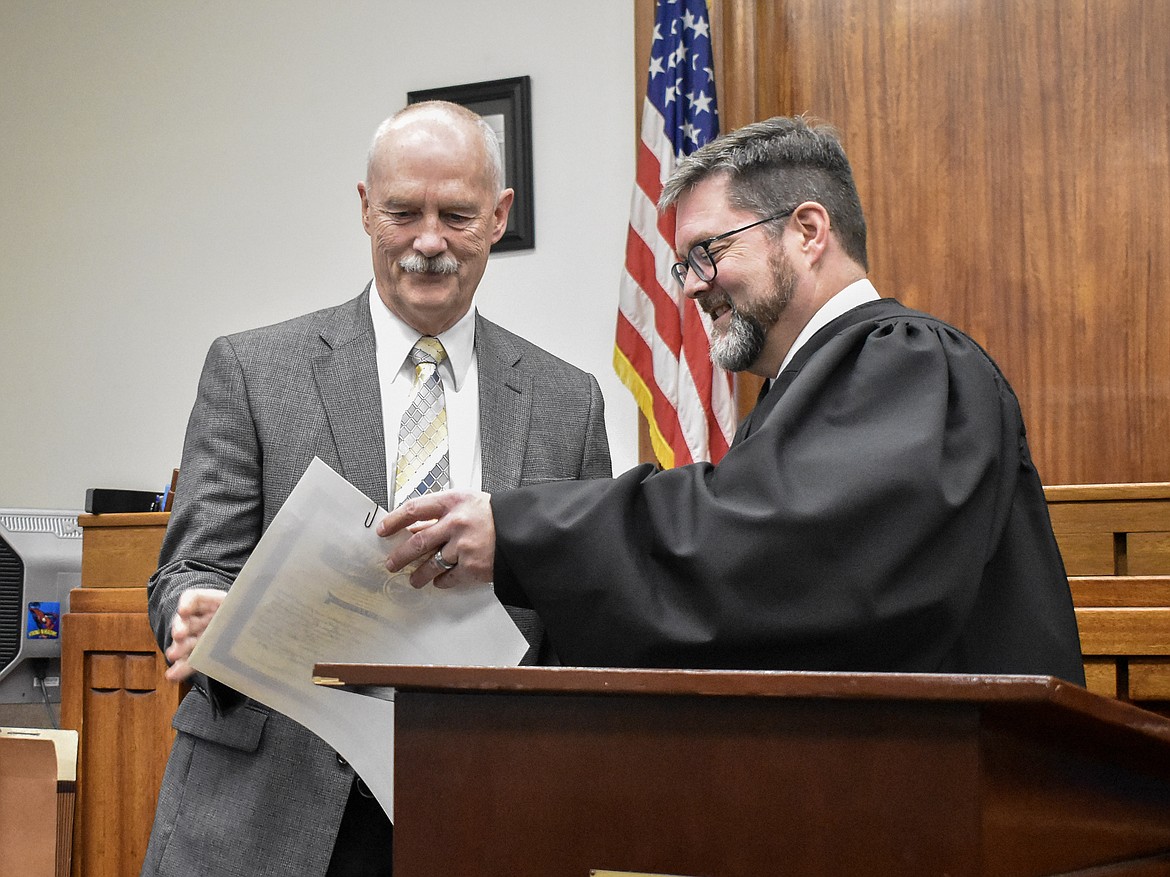 Montana 19th Judicial District Judge Matt Cuffe hands Lincoln County Coroner Steven Schnackenberg his papers to sign after his swearing in at the County Courthouse Wednesday. (Ben Kibbey/The Western News)