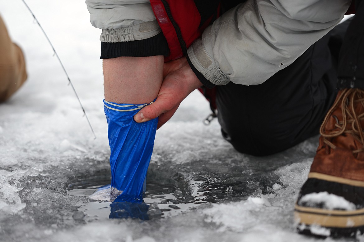 Jacob Steinle, of Creston, covers his hand and arm with a plastic bag to help his brother Samuel reel in a fish without breaking the line on the edge of the ice at the Sunriser Lions ice fishing derby at Smith Lake on Saturday. The fish ultimately snapped the line and got away. (Casey Kreider/Daily Inter Lake)