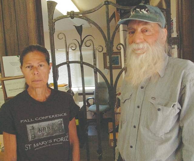 TERRY AND Jean Melton of Plains stand in front of the iron gate inside the Plains Library. Terry and other members of the Northern Rockies Blacksmith Association constructed the gate, which was installed in 2006. The Meltons were on hand to celebate the 100th anniversary of the opening of the Plains Library on Saturday, Aug. 18. (Joe Sova/Clark Fork Valley Press)