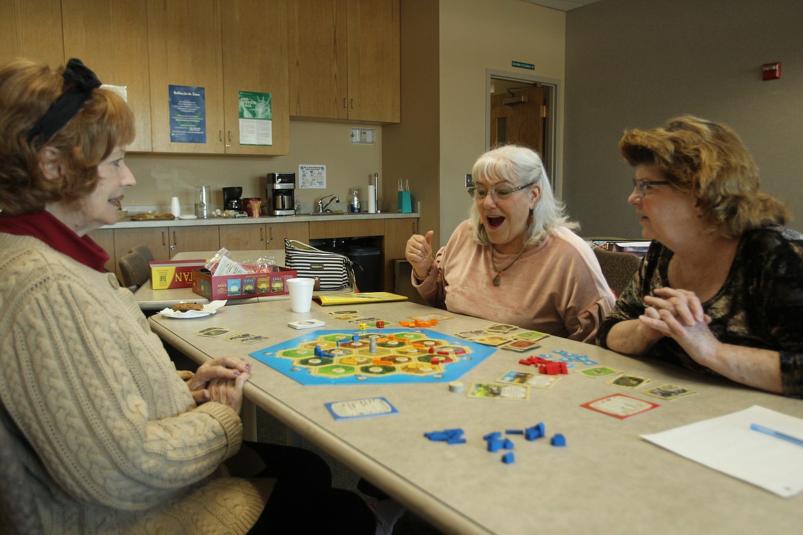 DEVIN WEEKS/Press
Paula Leinweber, center, is delighted to roll the first 12 of the game as she plays Catan with new friends Carla Langdon, left, and Donna Smith in the Post Falls Library on Saturday.