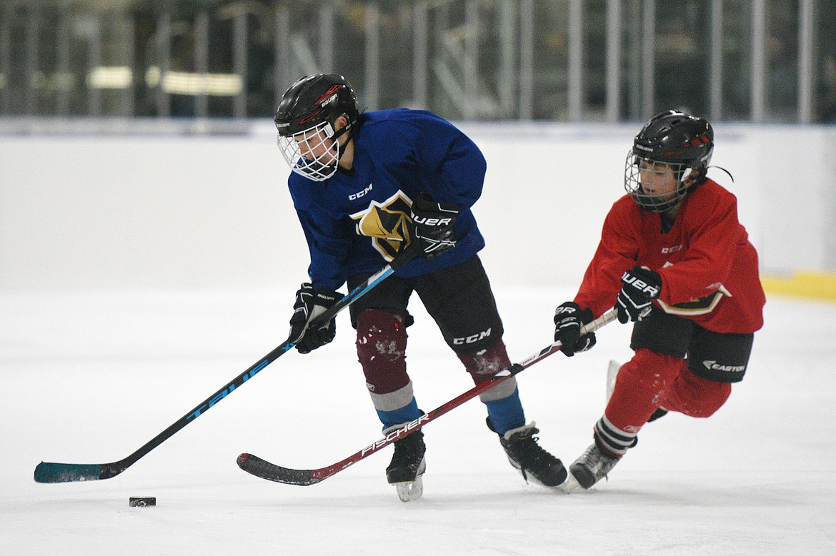 A blue team player skates with the puck against a red team defender.