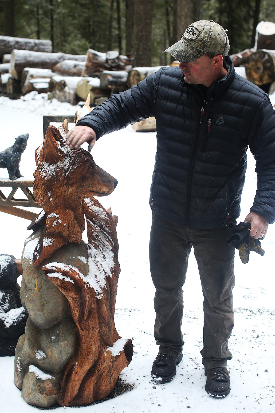 Jeff May brushes snow from one of his art pieces that was saved from the fire at his wood shop in Athol.