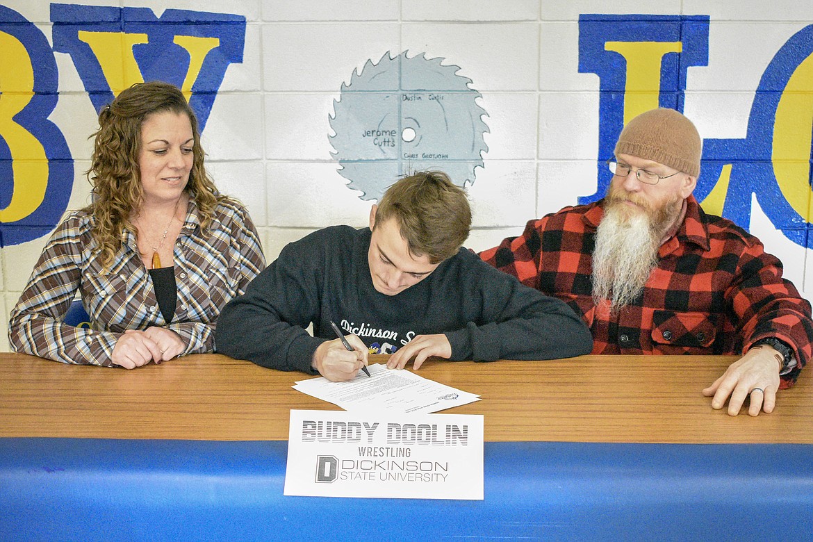 Libby High School senior Buddy Doolin signs to wrestle at Dickinson State on Wednesday while parents Jessica Doolin and Darrell Vanderhoef look on. (Ben Kibbey/The Western News)
