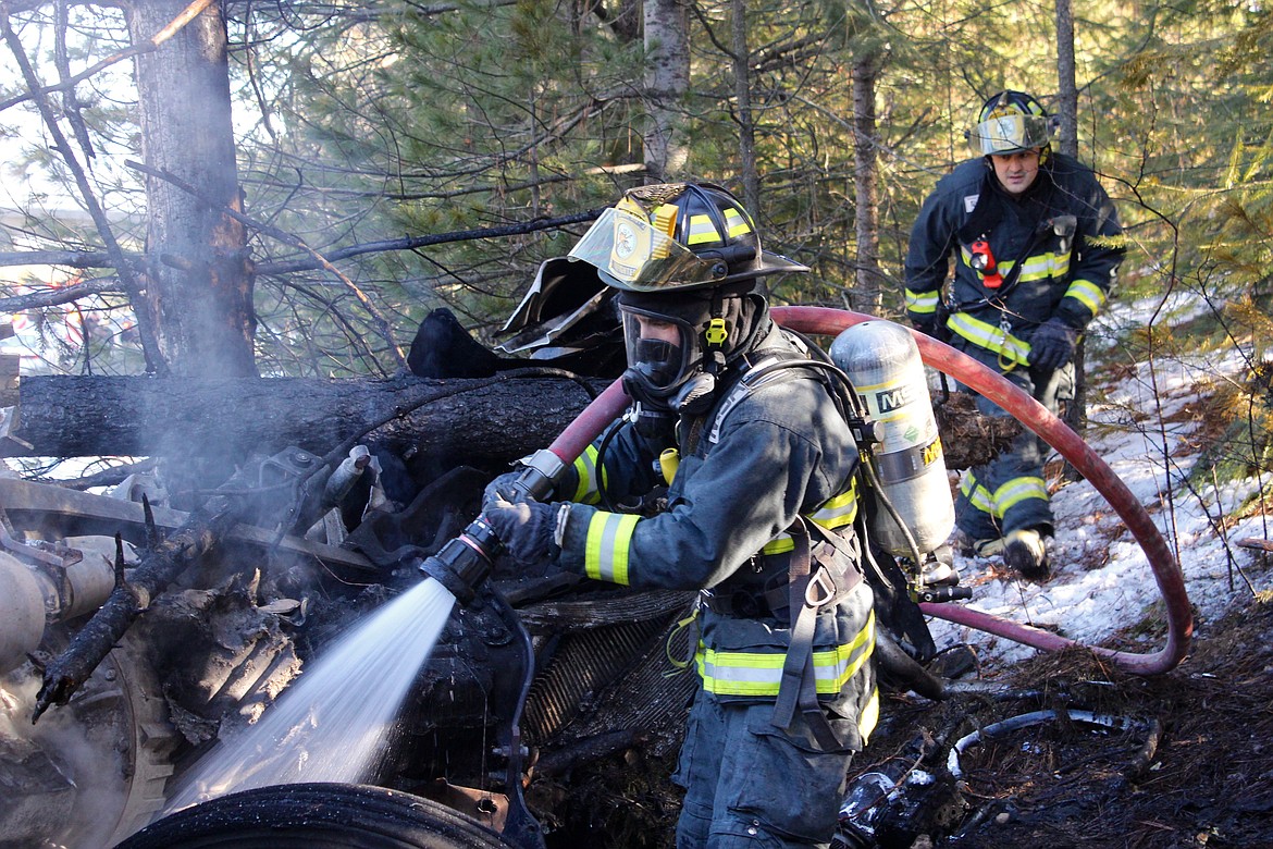 Shoshone County Fire District No. 2 firefighters/EMTs Sam Rodier (left) and Lavoryn Nguyen hose down the area and survey the damage of the wreck.