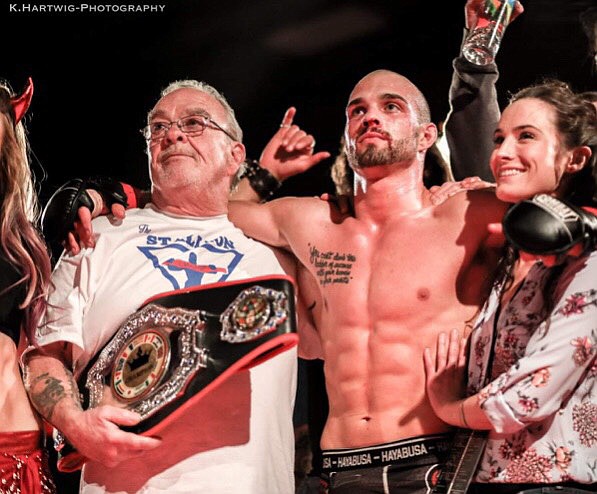 Craig Feistner is pictured just after accepting the belt for winning an MMA Cage Combat Championship at 155 pounds. Holding the belt is his trainer Pablo Alfonso. (Photo courtesy of K.Hartwig Photography)