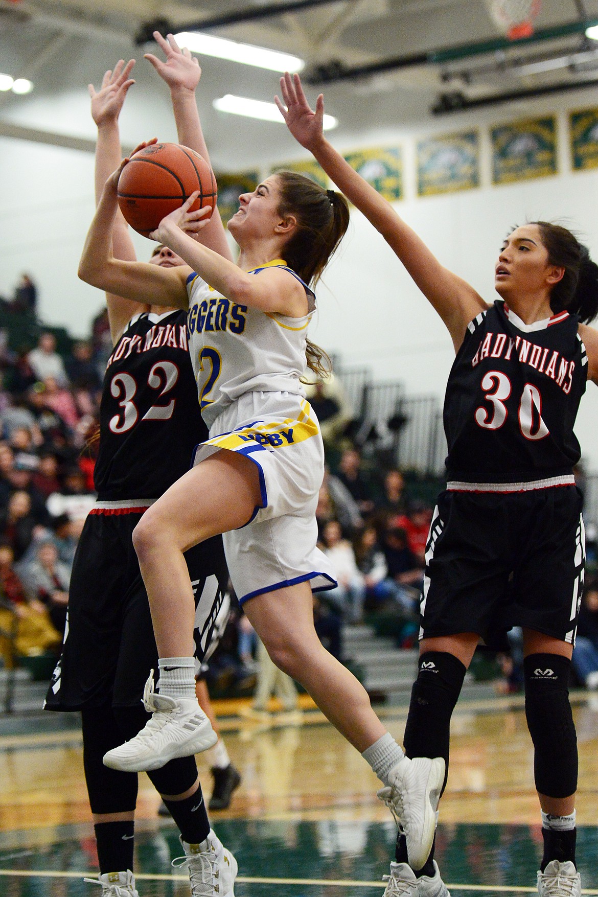 Libby's Alli Collins (12) drives to the basket against Browning's Taylor Jordan (32) and Dulci Skunkcap (30) at Whitefish High School on Friday. (Casey Kreider/Daily Inter Lake)
