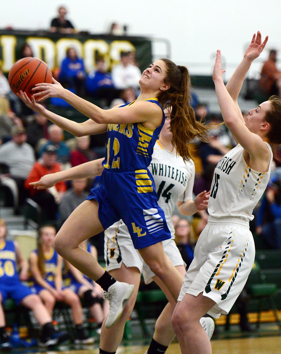 Libby's Alli Collins (12) drives to the basket with Whitefish's Gracie Smyley (14) and Payton Kastella (15) defending at Whitefish High School on Thursday. (Casey Kreider/Daily Inter Lake)