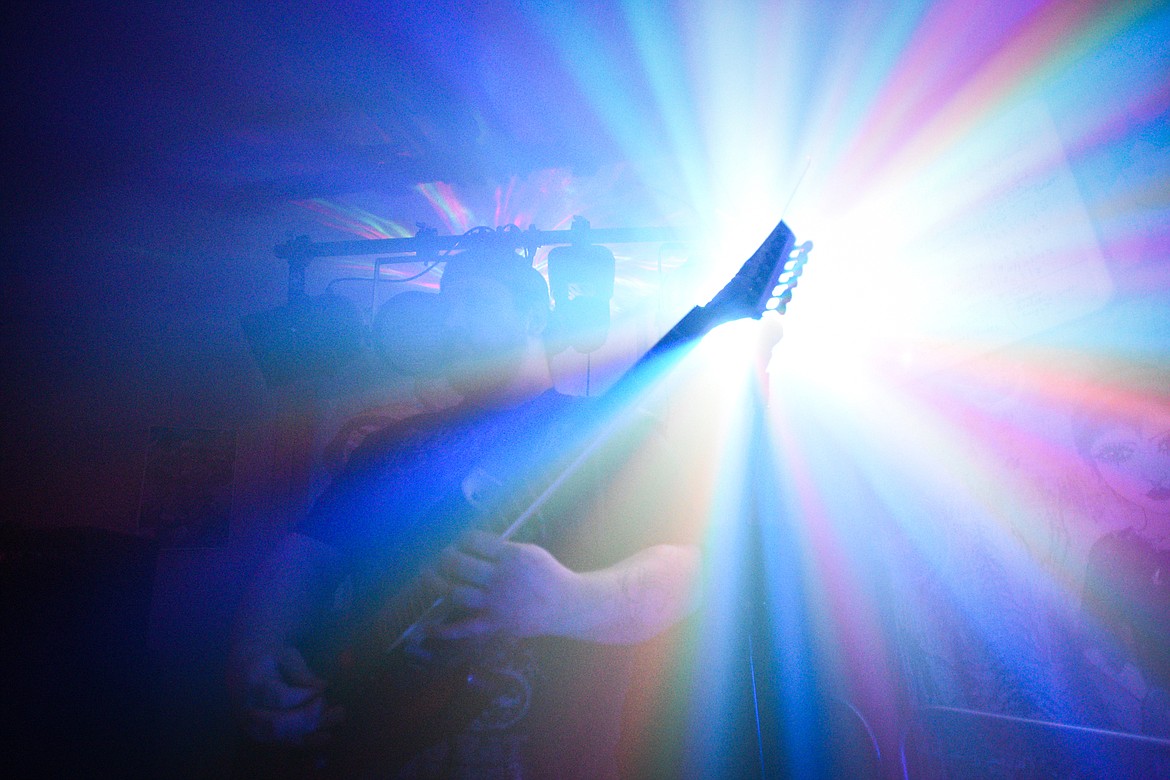 A stage light shines through the headstock of a bass guitar while Undying Avarice plays.