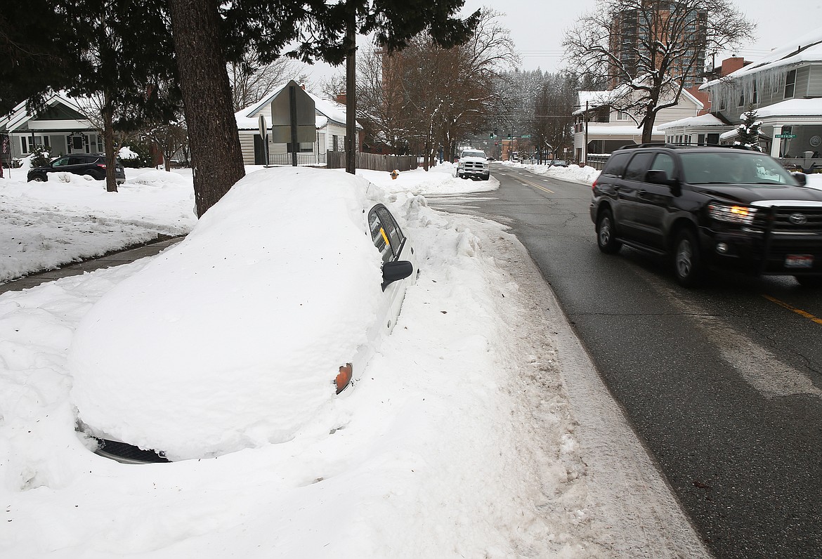 A motorist turns north on Seventh Street by a snowed in car with a 48-hour notice for removal posted on the driver side window. (LOREN BENOIT/Press)