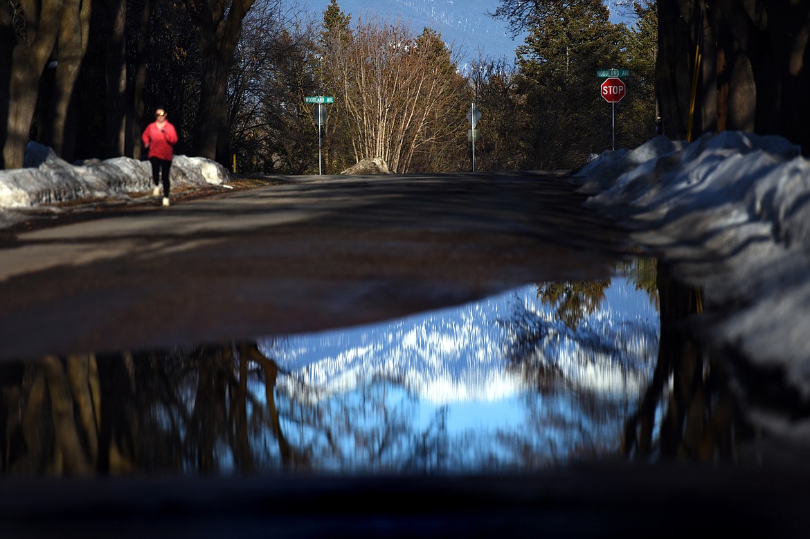 The Swan Range is reflected in a puddle of snow melt as a jogger runs along 5th Street East in Kalispell on Wednesday, March 20. (Casey Kreider/Daily Inter Lake)