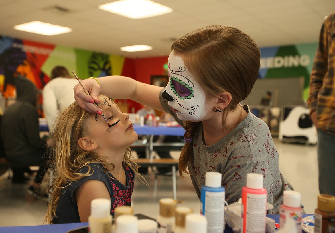 Wearing Latin sugar skull paint, Izzy Lilley, 11, of Coeur d'Alene, traces a unicorn outline on 6-year-old Magnolia Meyer's face Saturday during the 10th annual Community Multicultural Faire in Lakes Magnet Middle School. (DEVIN WEEKS/Press)