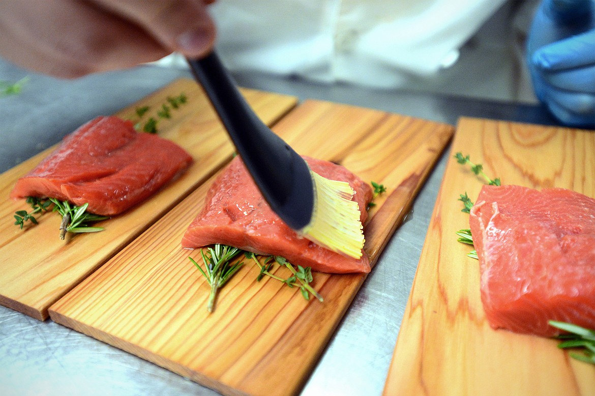 Eli Valadez adds a baste to his salmon over a rosemary and thyme garnish inside the kitchen at the Culinary Institute of Montana at Flathead Valley Community College on Wednesday, April 3. (Casey Kreider/Daily Inter Lake)