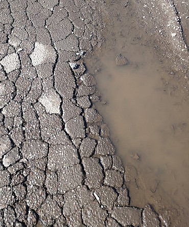 EVERY WHEEL that rolls over a saturated, softened street causes further surface degradation. Note the pool of water that damages pavement.