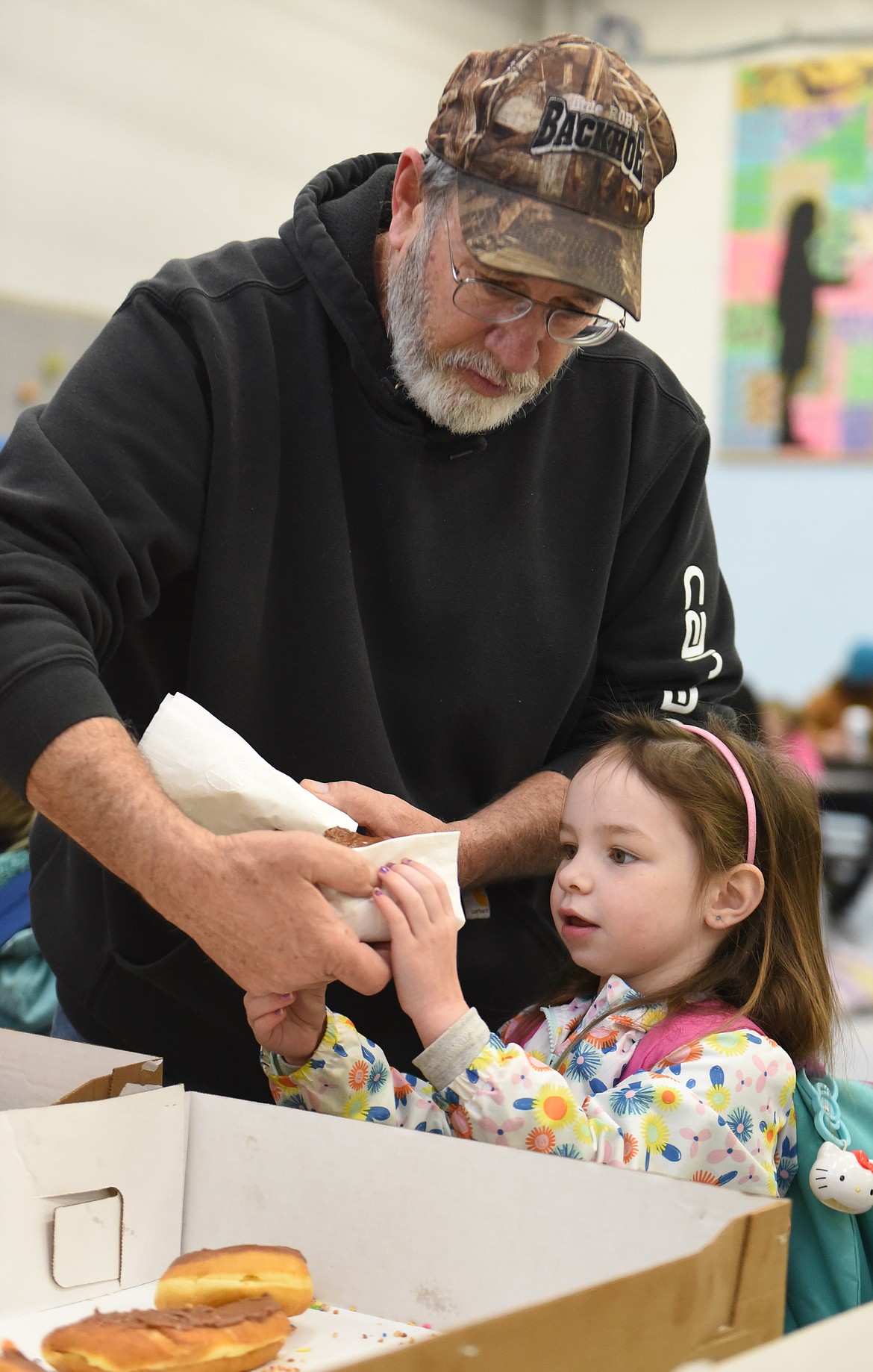 BRENT SLIKER helps pre-school granddaughter Brooklynn Johnson handle a donut during the April 12 event that filled the CVE lunchroom.