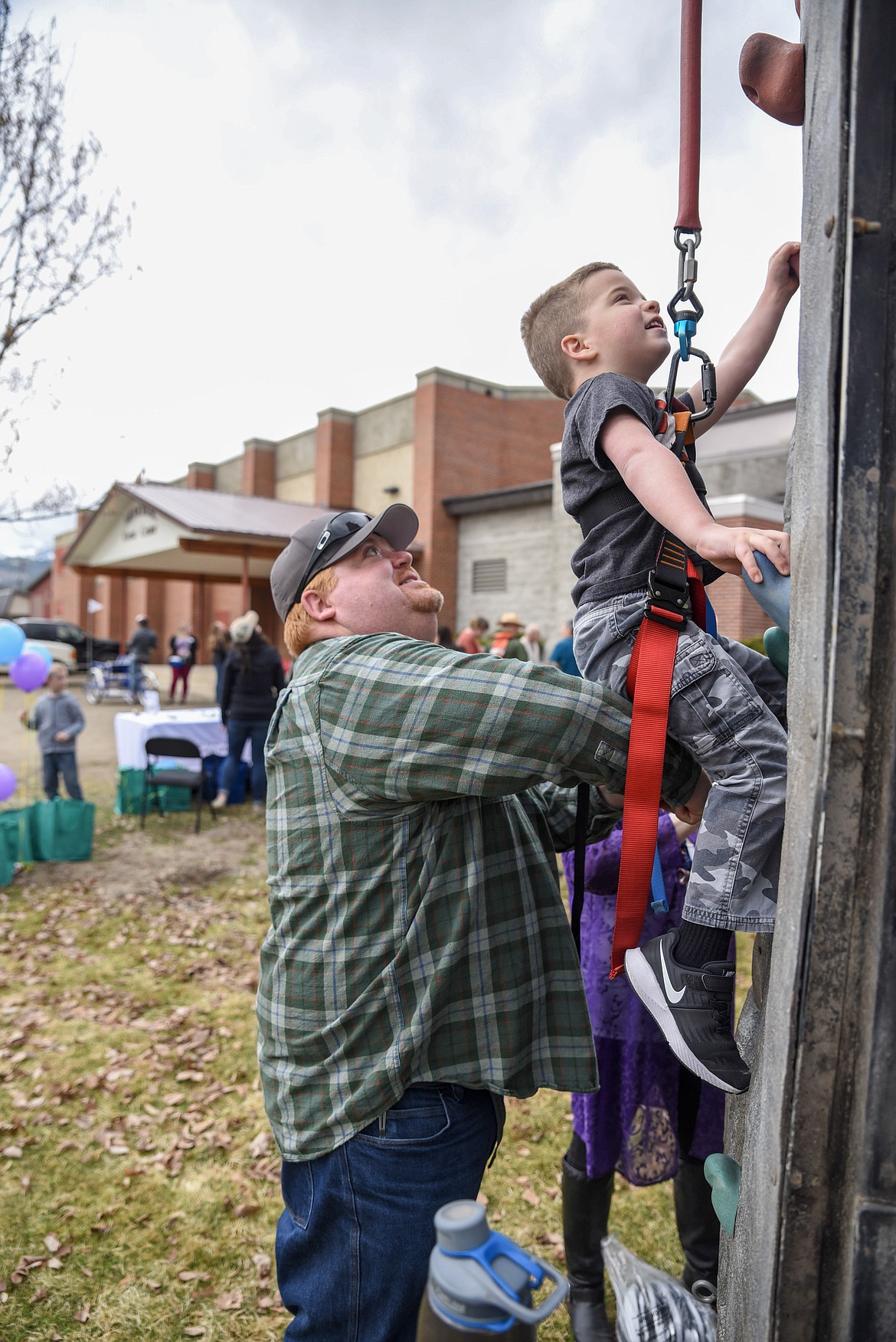 Sam Scheer helps his son, Ben, on an attempt at the climbing wall at the Cabinet Peaks Medical Center Annual Health Fair at the Libby Memorial Events Center on Saturday. (Ben Kibbey/The Western News)